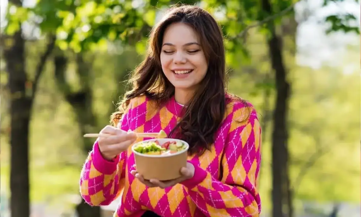 Woman enjoying a nutritious poke bowl in NYC park, showcasing vibrant, fresh ingredients.