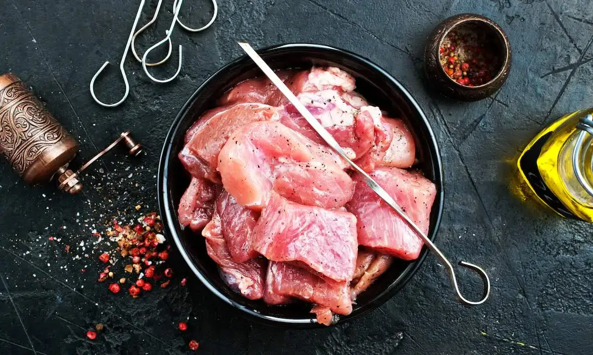 Raw cubed pork with a metal skewer and spices for poke bowl