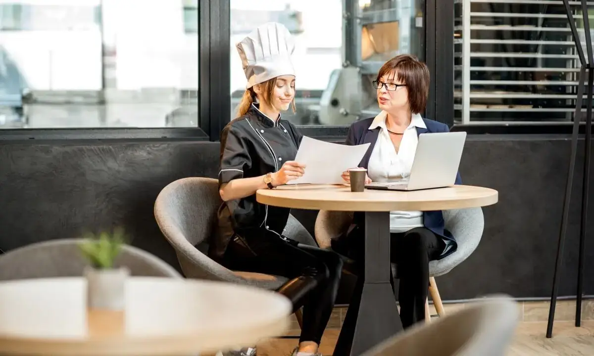 Chef and businesswoman reviewing franchise paperwork at cafe table