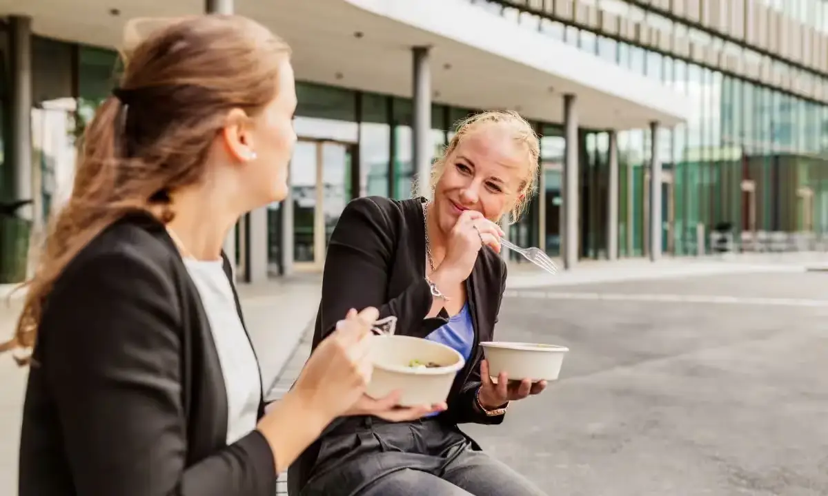 Two colleagues enjoying poke bowls outside a modern office building